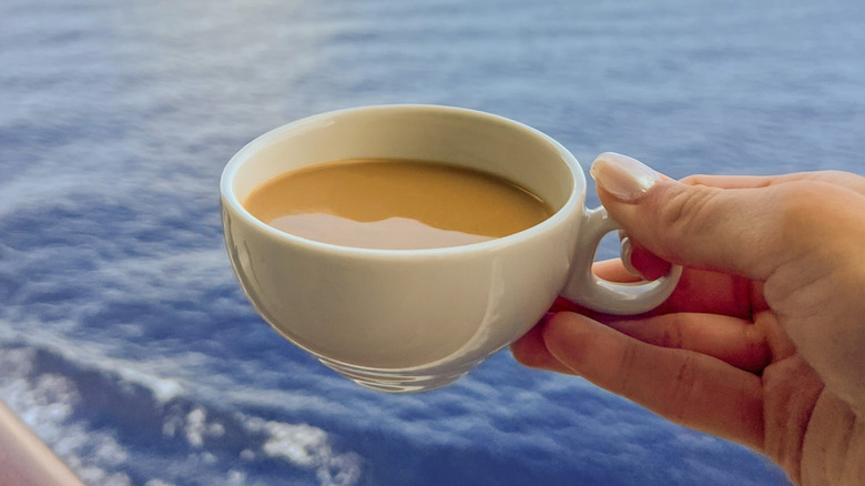 Manicured female hand holding a white ceramic demitasse cup of coffee with ocean in the background on a ship deck