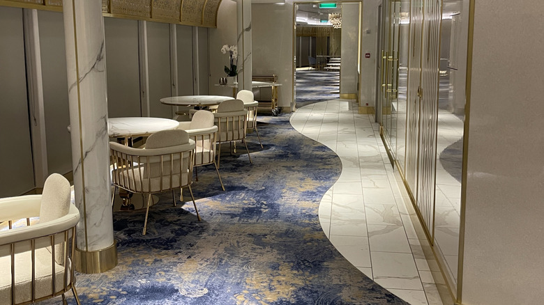 Interior view of Enchante specialty dining restaurant on the Disney Wish ship with gold and blue carpeting, cream chairs, gold accents, and marble tables