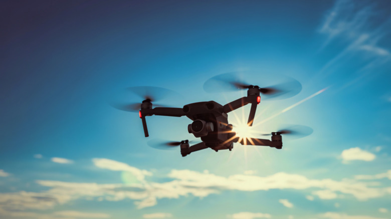 A dark silhouette of a quadcopter drone against a vibrant blue sky