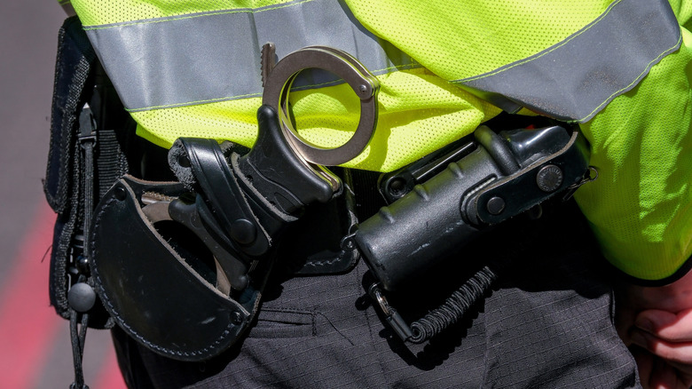 Metropolitan Police officer wearing a high visibility jacket, with close up of handcuffs and section 5 weapon pepper spray in London, UK.