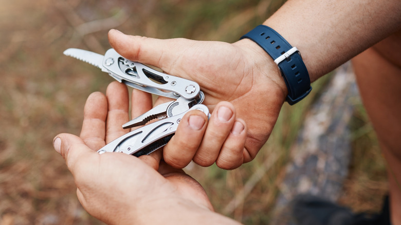 Close up of man's hands holding a Swiss Army-type multiple tool that includes a pocketknife