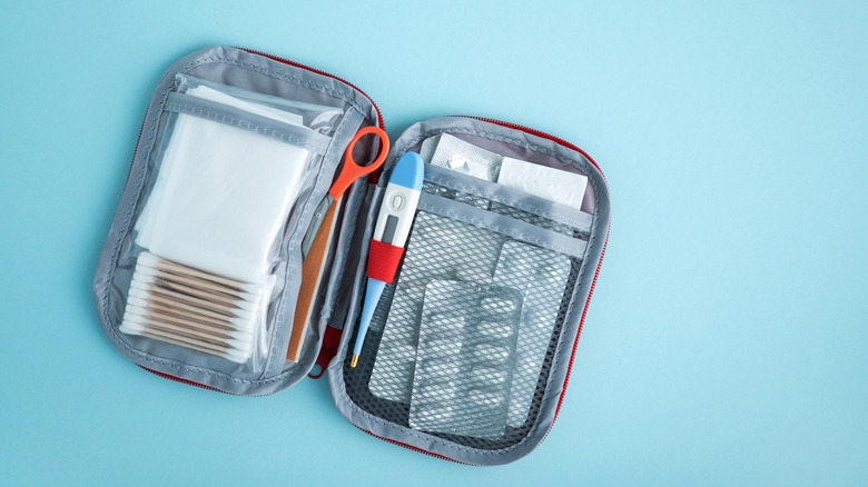 Travel first aid kit organized with medical supplies including bandages, cotton swabs, tweezers, scissors, thermometer, and blister packs.