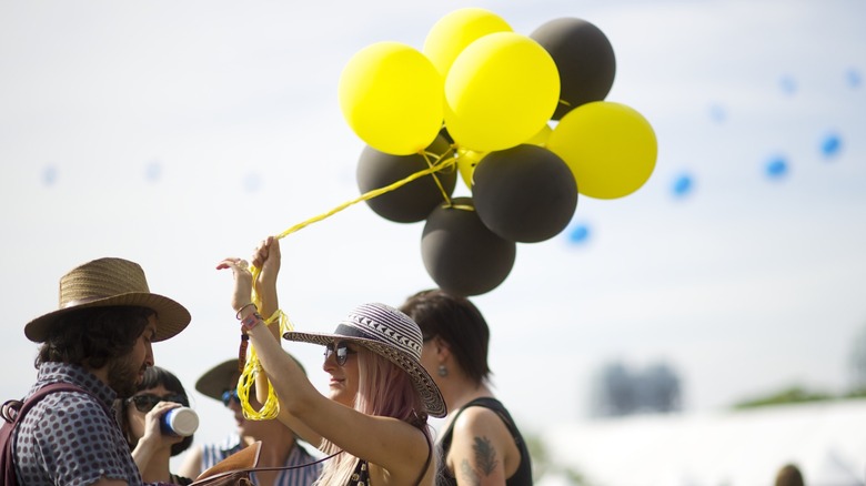 A group of friends including a woman holding yellow and black balloons