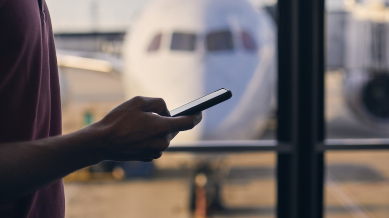 Personal standing by airport gate window looking at their phone