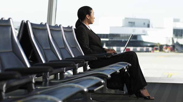 Woman in suit sitting at empty airport gate on her laptop