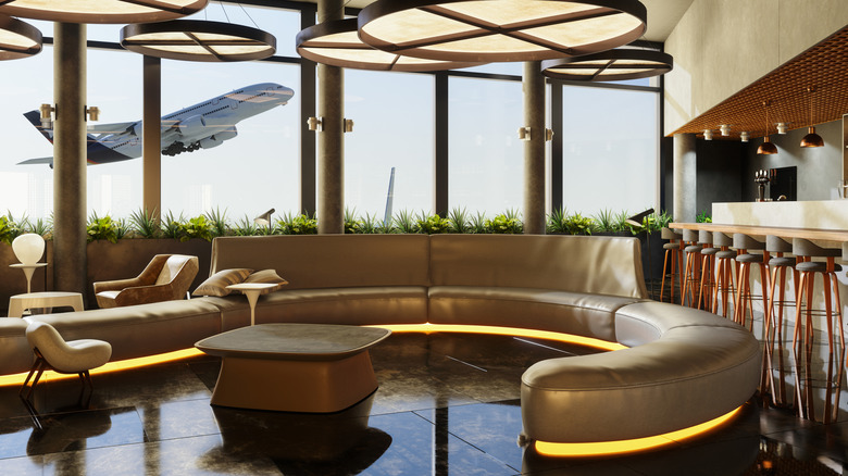View of U-shaped couch and bar at an airport lounge with plane taking off