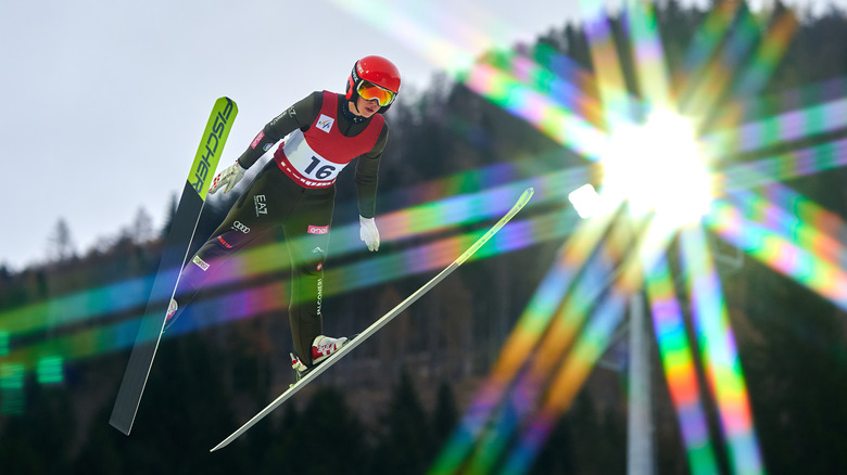 a ski jumper flies in the air towards a lens flare