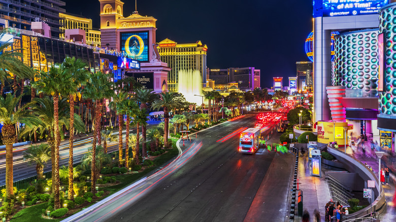Light trails from cars on Las Vegas Strip at night with palm trees.