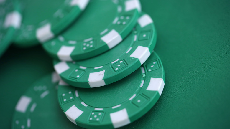 Green casino poker chips on green gaming table close up.