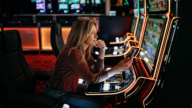 Women gambling on slot machinery holding a cell phone