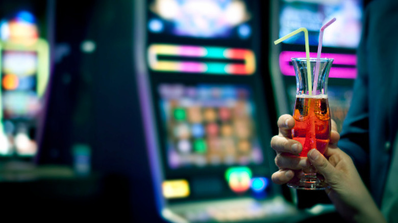 A man giving a cocktail to a woman, only hands visible. Slot machines in the background.