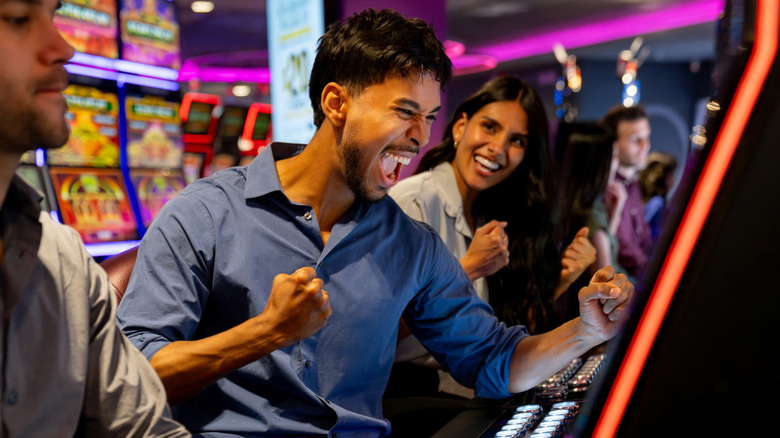 Excited Latin American man celebrating while winning on a slot machine at a casino.