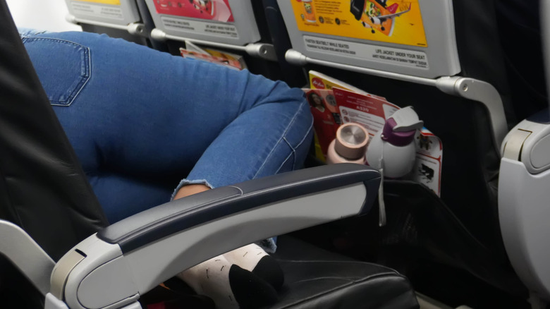 A sock-footed female passenger sleeps on three seats on a plane.