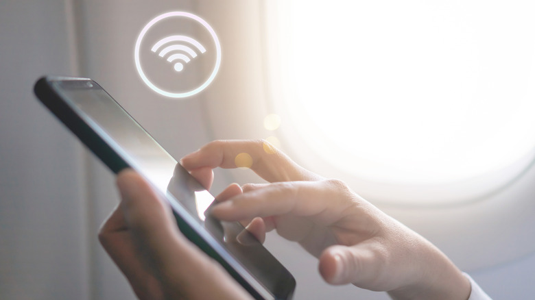 Woman's hand using smartphone with WiFi icon floating above phone with airplane background