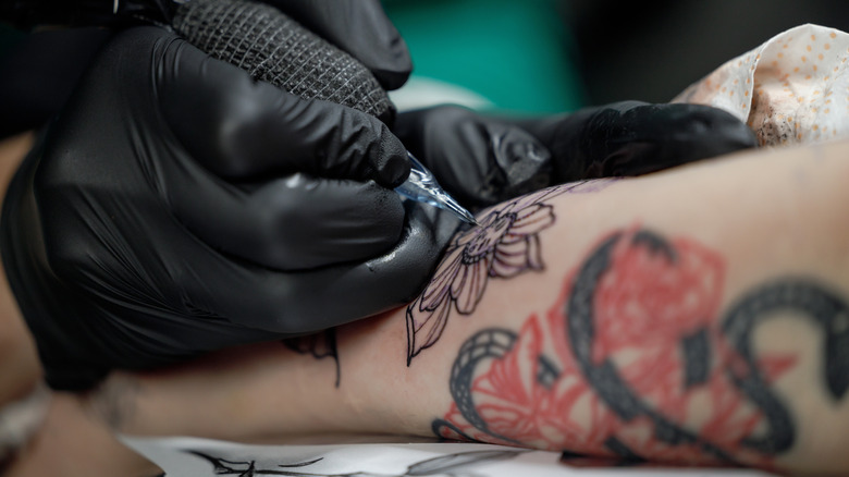 Close-up of tattoo artist wearing black gloves doing floral work on a Caucasian forearm