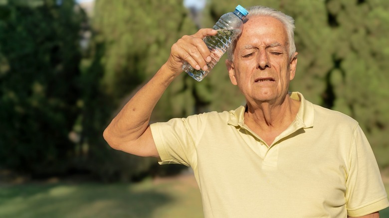A senior citizen man cooling his head with a water bottle in the summer heat