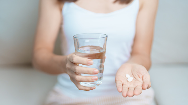 A woman holding aspirin and a glass of water