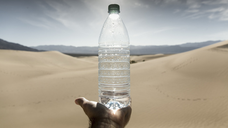 A hand holds a plastic bottle of water in front of the sand dunes at Death Valley