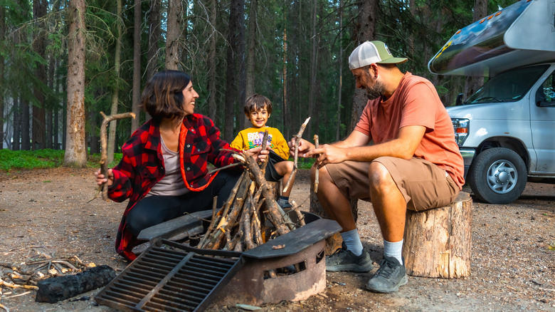Family enjoying camping, preparing a campfire next to their campervan