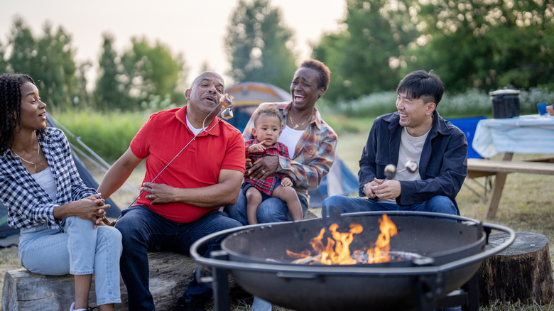A family of five sit around a fire during a family camping trip as they roast marshmallows together