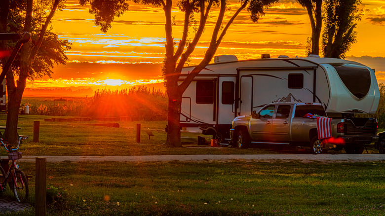 Fifth wheel RV and truck parked at campsite with sun setting in background