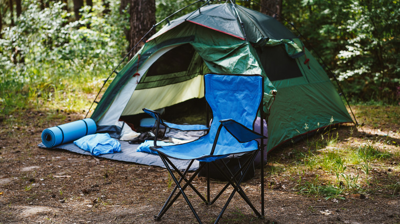 A blue folding chair stands before a green camping tent with a sleeping mat