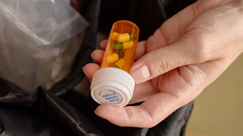 A hand holding a prescription bottle full of pills