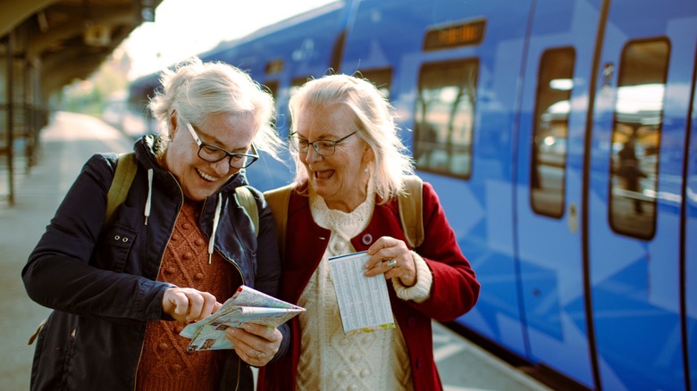 Two women looking at a paper while standing next to a train