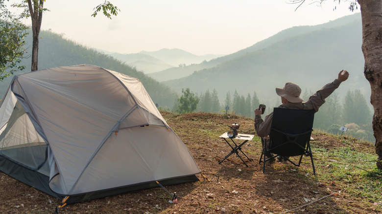 A solo male traveler stretching in a camping chair next to his tent.