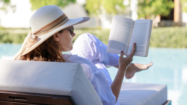 A tourist reading a book while sitting by the swimming pool.