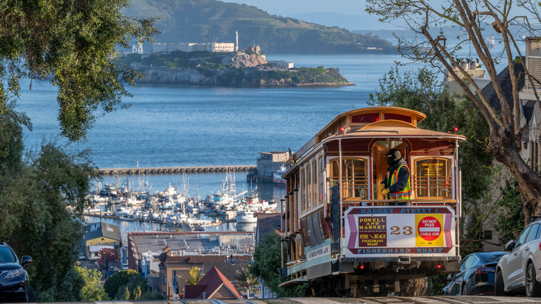 A cable car on top of a hill in San Francisco in the morning with a long view over Alcatraz