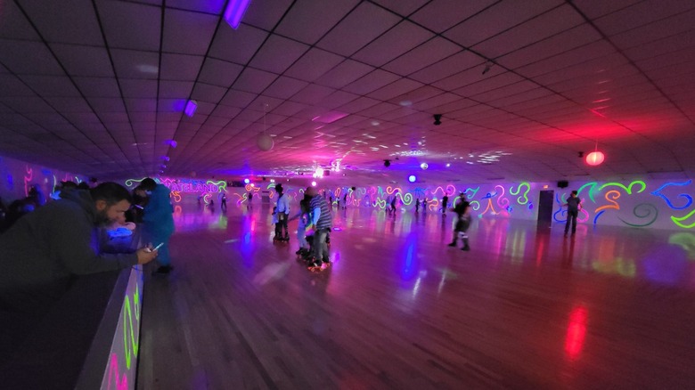 People roller skate beneath neon lights at Skateland Rocks.