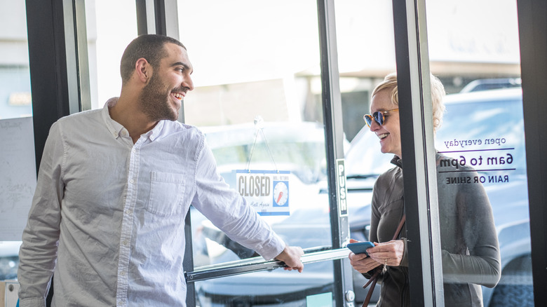 Smiling man holding a door open for a woman