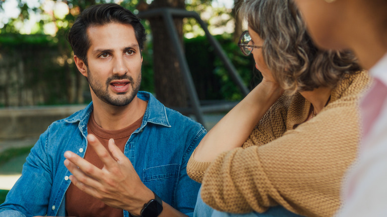 A man on the street talking while two women listen intently