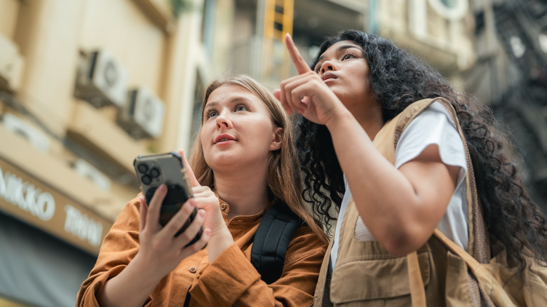 Woman giving directions to another woman who us holding a smartphone on the street