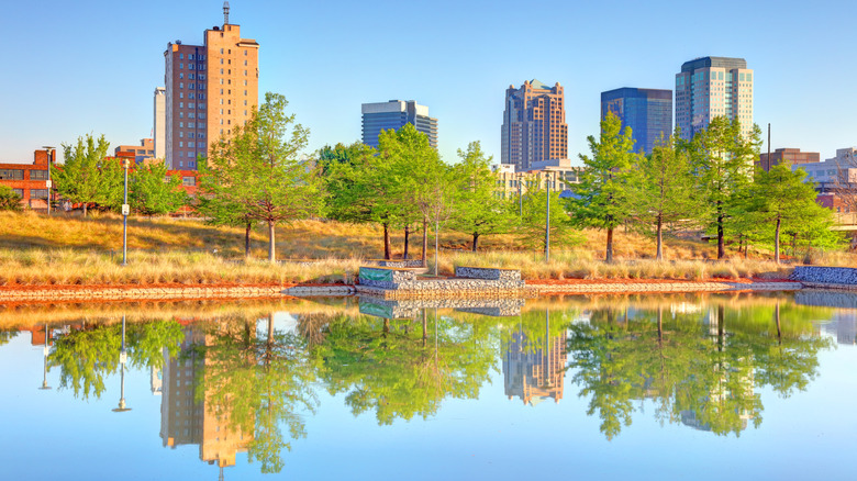 The Birmingham, Alabama, skyline behind a river with the trees and buildings reflected on the water