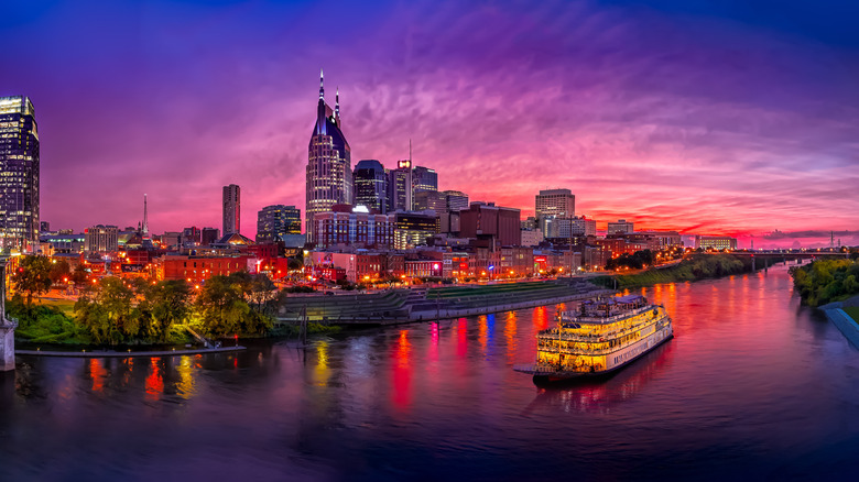 The skyline of Nashville at night with lights reflected in the river and a cruise ship on the water