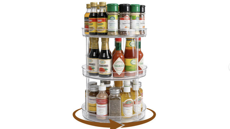 View of three-tier acrylic Lazy Susan storage unit filled with spices and condiments on white background