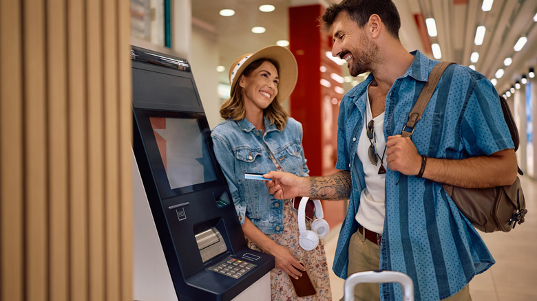 A smiling couple using an airport ATM