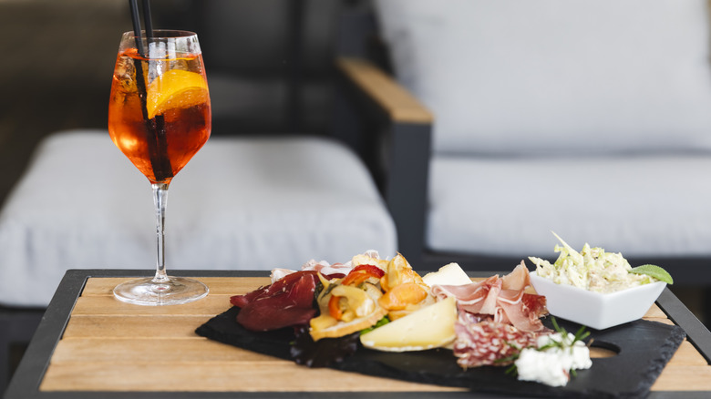 Aperol spritz next to a charcuterie board with meat, cheese, and vegetables on a table