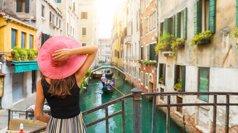 Tourist in a pink hat looking over a canal in Venice, Italy