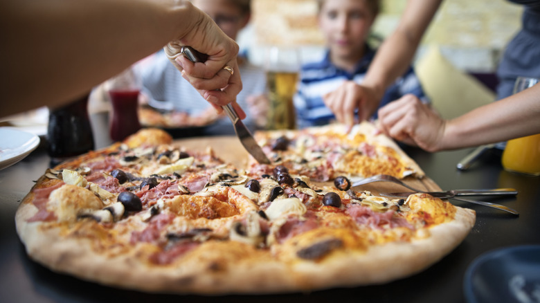 People cutting a pizza with a knife and fork