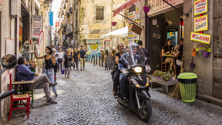 People riding a motorcycle through a busy street in Naples, Italy