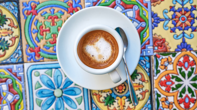 Small coffee with a saucer and spoon on a colorful, tiled table