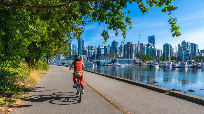 On a sunny summer day, a woman enjoys a leisurely bike ride along the seawall in Stanley Park, Vancouver