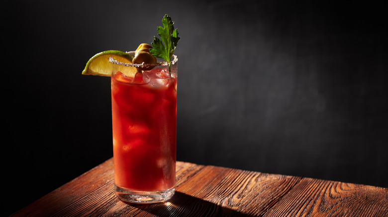 Iced bloody Mary (Caesar) cocktail in a glass, rimmed by salt and pepper on a wooden bar and dark background