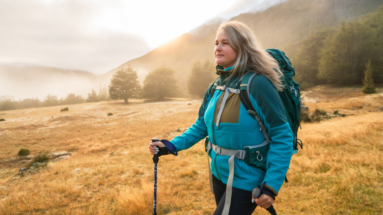 Woman in winter clothing, exploring the wilderness, holding hiking poles and wearing a backpack