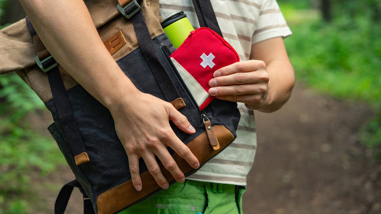 Close-up of a person taking a first aid kit out of a backpack while on a forest trail