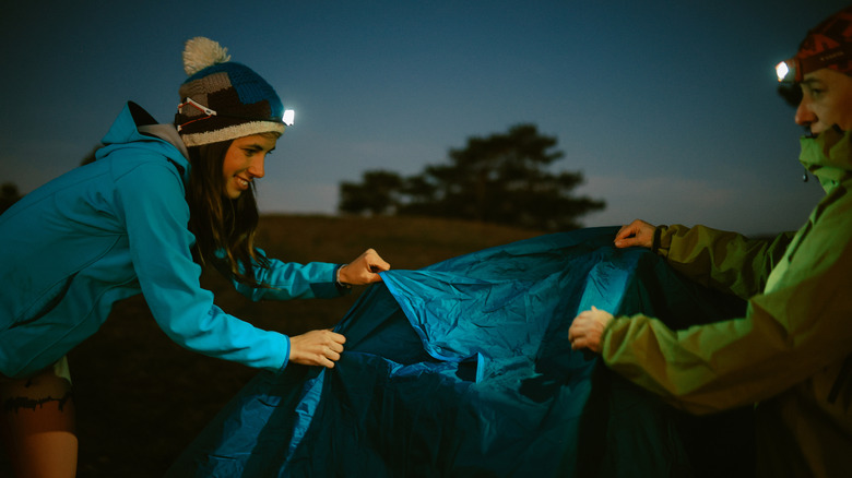 Two people wearing headlamps putting up a tent