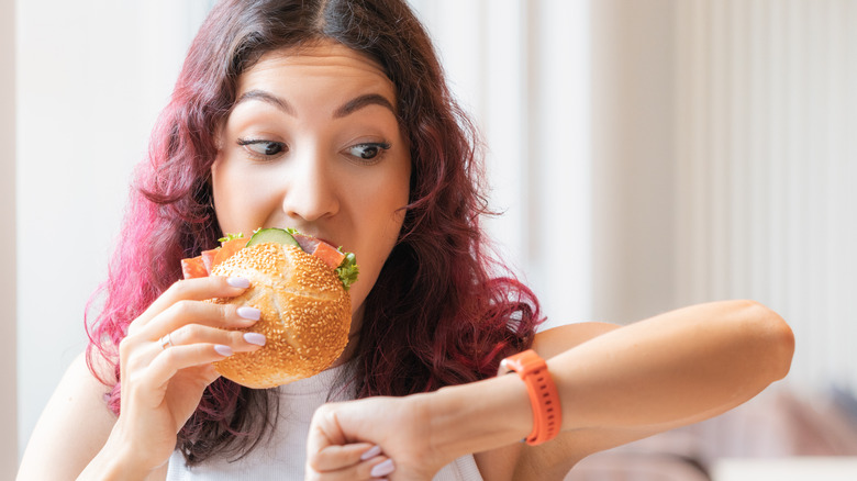 Woman eating in a hurry while checking watch
